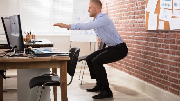 Man taking a break while working. doing squat behind his desk. 