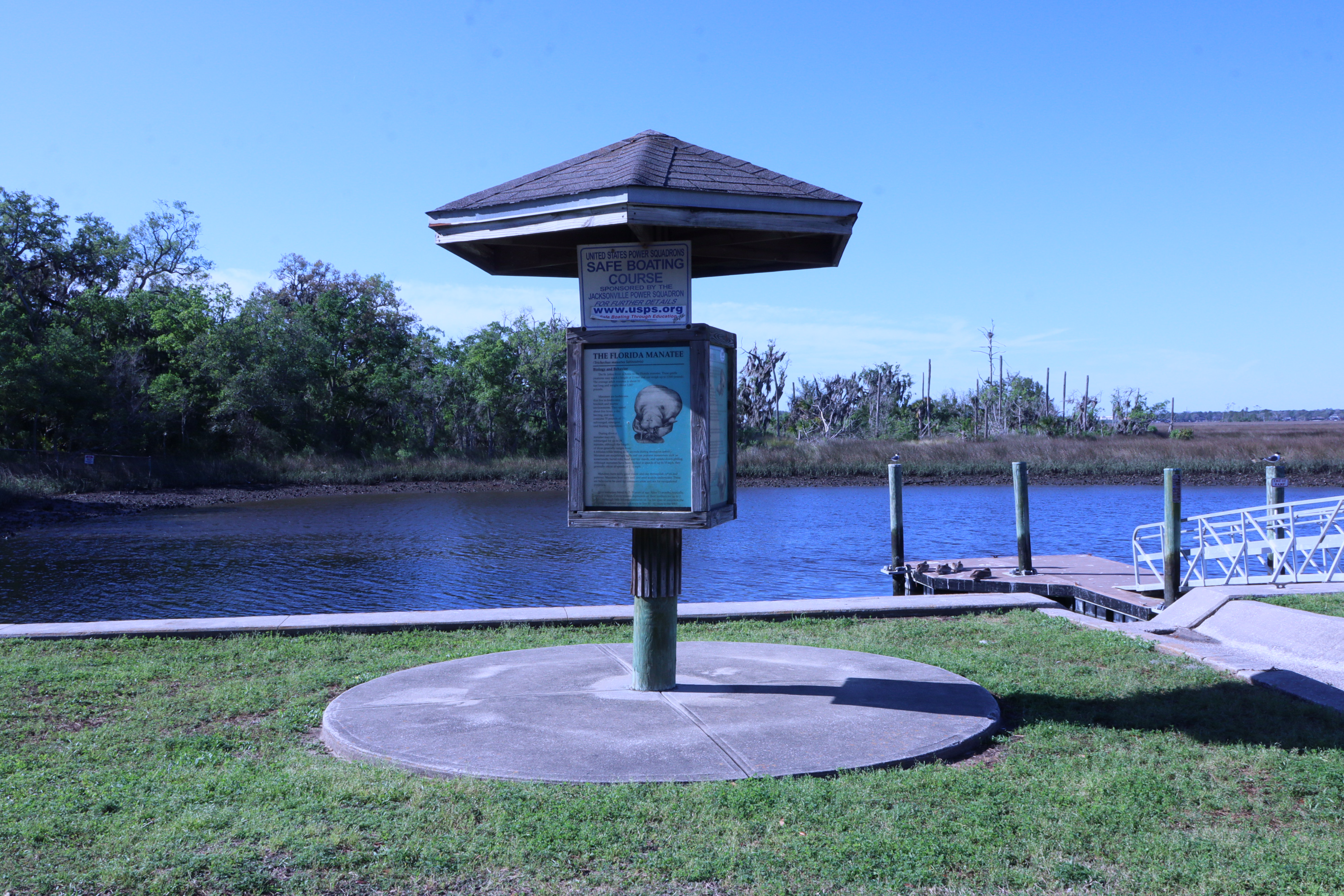 Manatee education post on a concrete slab overlooking a canal and a gangway to a pier