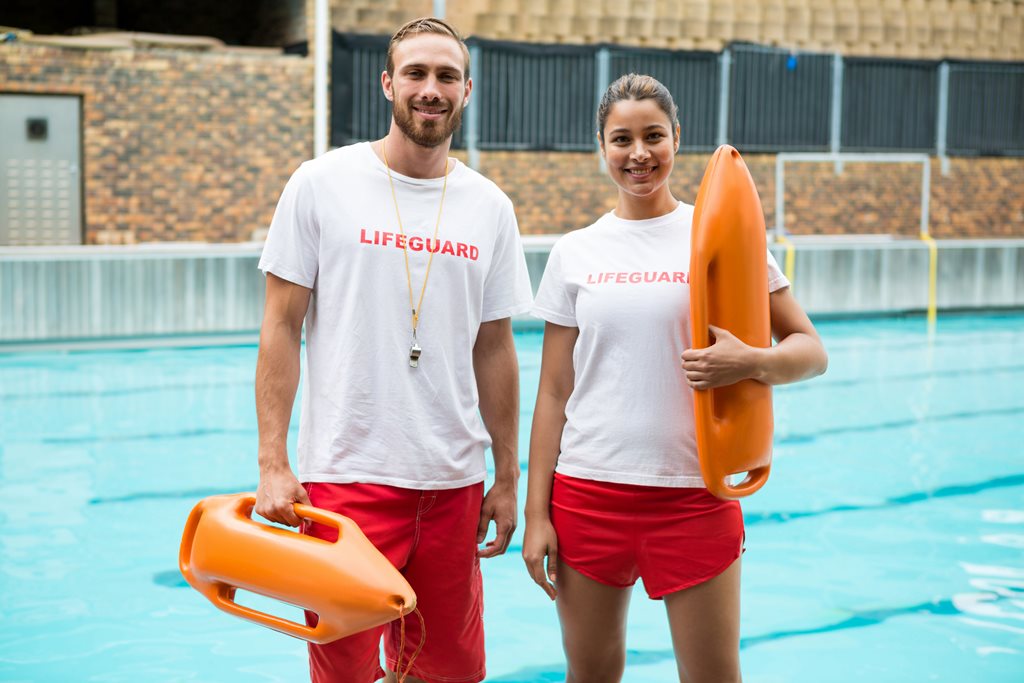Portrait of two lifeguards standing with rescue buoy at poolside