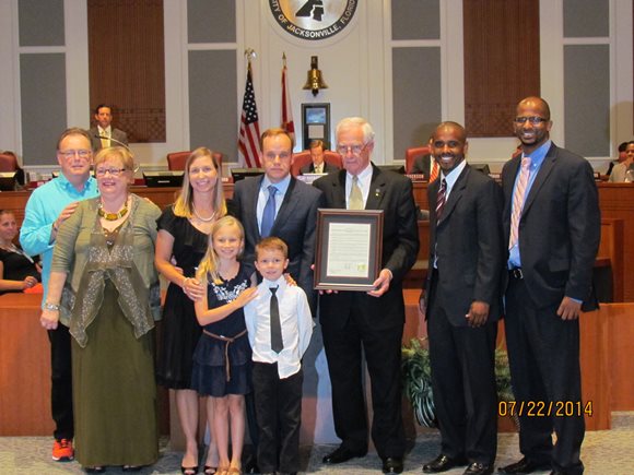 July 22, 2014 photo of Council Member Bill Gulliford  presenting Pastors Michael and Connie Smith a framed resolution commending them for community work in lauching the 