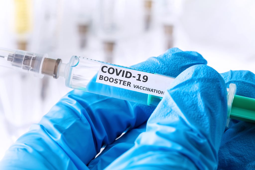 gloved hand holding COVID booster vaccination needle