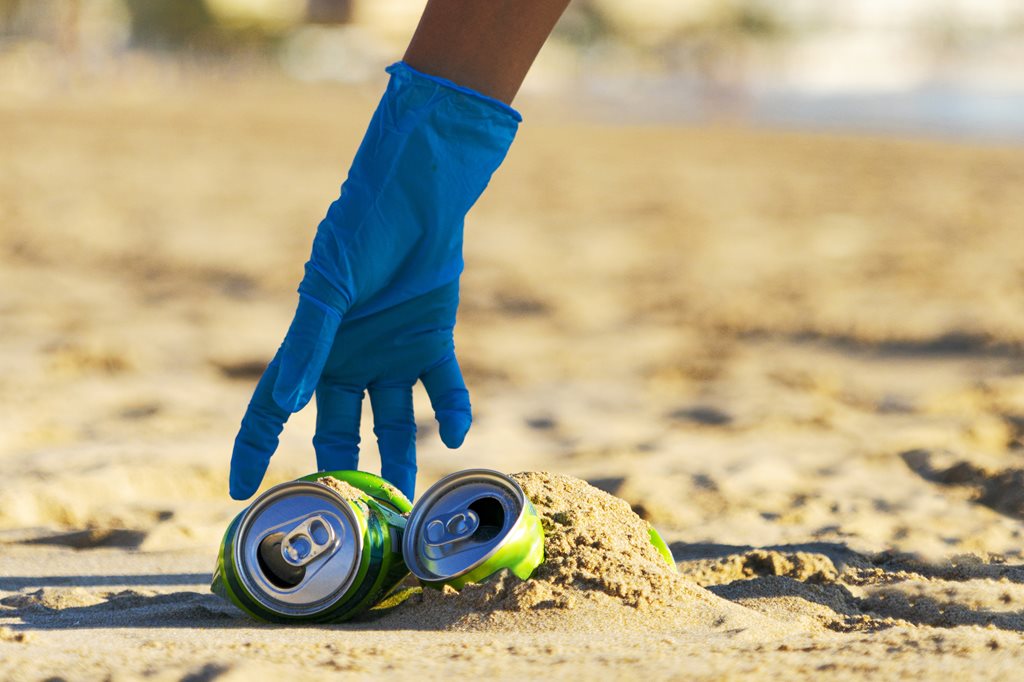hand picking up empty soda can on beach