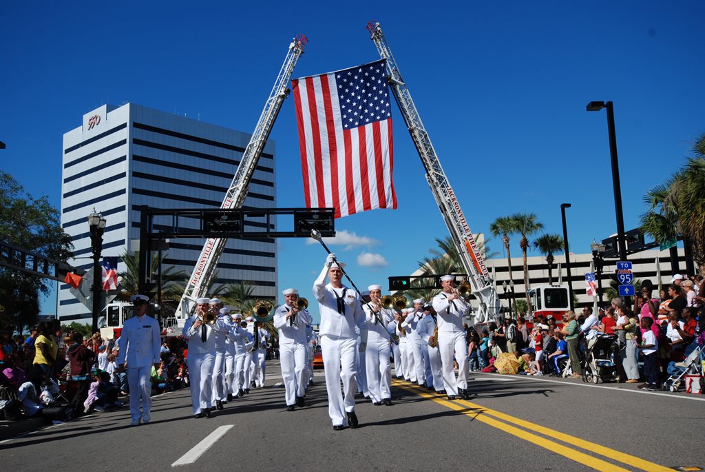 navy officers walking under an american flag during veterans day parade
