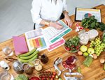 Woman writing on a planner with fruits and vegetables on top of the table
