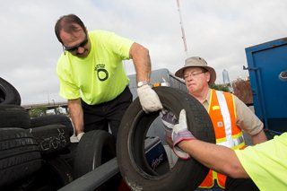 Photo of Council Member Crescimbeni lifting waste tires into a disposal container.