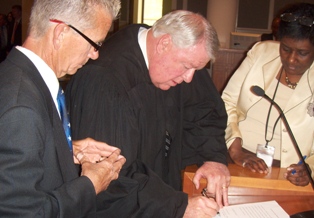 Photo of Chief Judge Donald Moran signing Council Member Doyle Carter's Oath of Office as he and Council Director Cheryl Brown look on.
