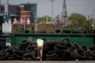 Photo of a worker resting against a large stack of tires.