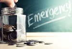 Hand placing coins in Jar in front of blackboard with the word Emergency written in chalk