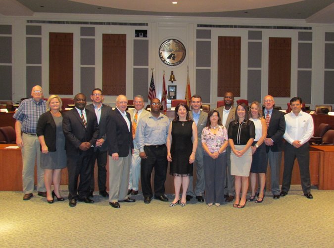 A photo of Task Force Members Jim Rinaman, Kerri Stewart, Paul Tutwiler, Michael Munz, Bill Mason, Steve Rohan, Opio Sokoni, Lori Boyer, Wyman Duggan, Kay Ehas, Broderick Green, Shannon Blankinship, Giselle Carson, Chuck Arnold, and Leon Carrero standing in the City Council Chamber.